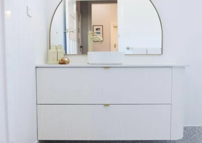 Modern bathroom with a floating white vanity, round mirror, small sink, and a woven rug on a speckled floor—perfect inspiration for bathroom renovations in Bunbury.