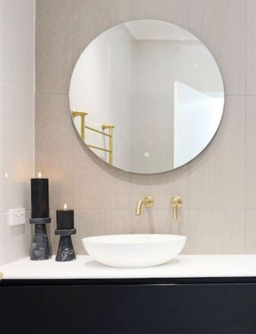 Modern bathroom with a round mirror, white vessel sink, gold faucet, and two black candle holders with lit candles on a white countertop. Modern bathroom with a round mirror, white vessel sink, gold faucet, and two black candle holders with lit candles on a white countertop.