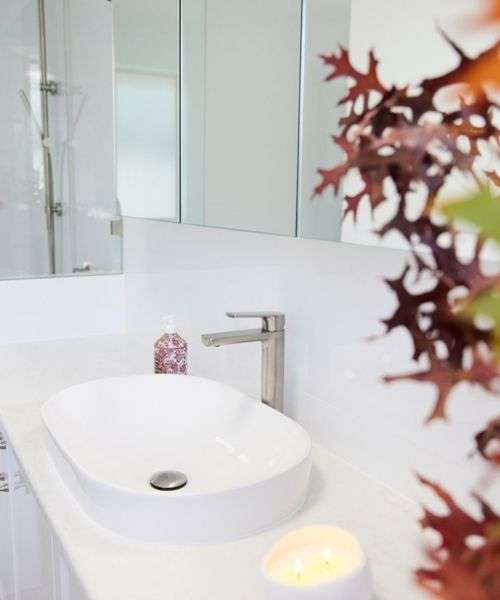 Modern white bathroom with a vessel sink, chrome faucet, soap dispenser, leafy plant, candle, and mirrored cabinet. Modern white bathroom with a vessel sink, chrome faucet, soap dispenser, leafy plant, candle, and mirrored cabinet.