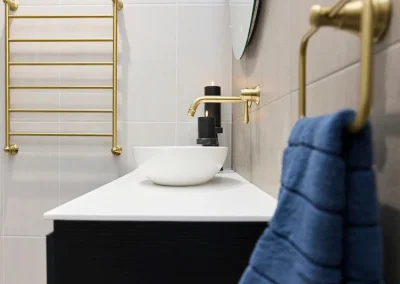 Modern bathroom with gold fixtures, a white vessel sink, black soap dispenser, round mirror, gold towel rack, and a blue towel hanging on a gold ring—perfect inspiration for your next bathroom renovation Bunbury.