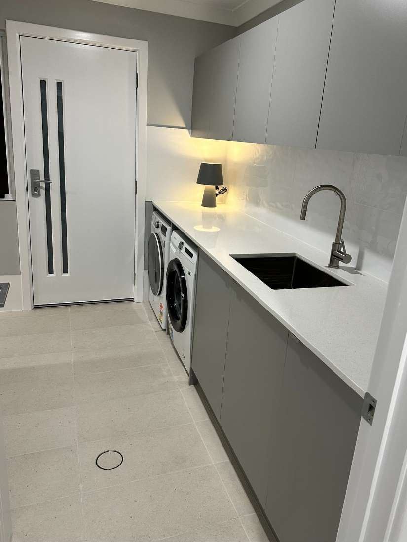 A modern laundry room with grey cabinets, a countertop sink, a front-load washer and dryer, under-cabinet lighting, and a white door. A modern laundry room with grey cabinets, a countertop sink, a front-load washer and dryer, under-cabinet lighting, and a white door.