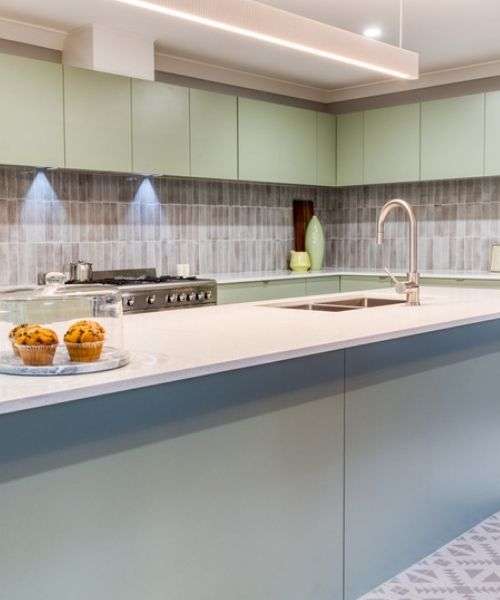 Modern kitchen with light green cabinets, stainless steel appliances, a sink island, and two muffins in a glass container on the countertop. Modern kitchen with light green cabinets, stainless steel appliances, a sink island, and two muffins in a glass container on the countertop.