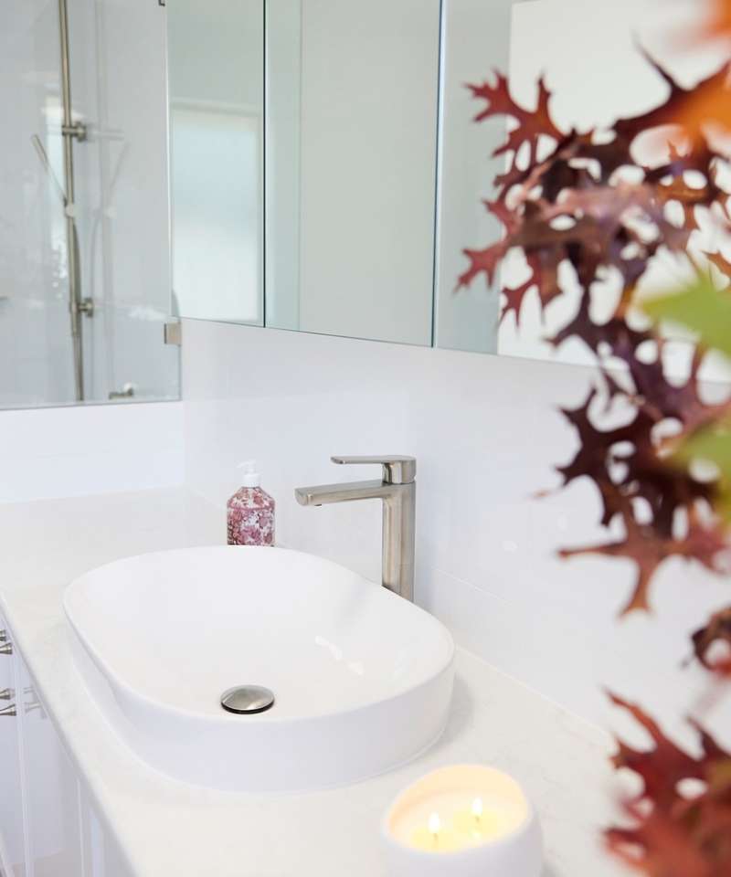A modern bathroom sink with a silver faucet, soap dispenser, burning candle, and a vase of autumn leaves on a white countertop. A modern bathroom sink with a silver faucet, soap dispenser, burning candle, and a vase of autumn leaves on a white countertop.